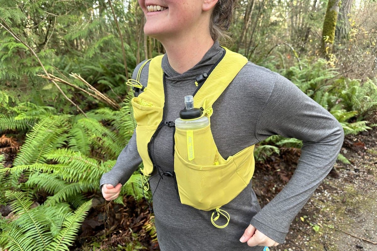 Runner wearing hydration vest on mountain trail with water bottles visible