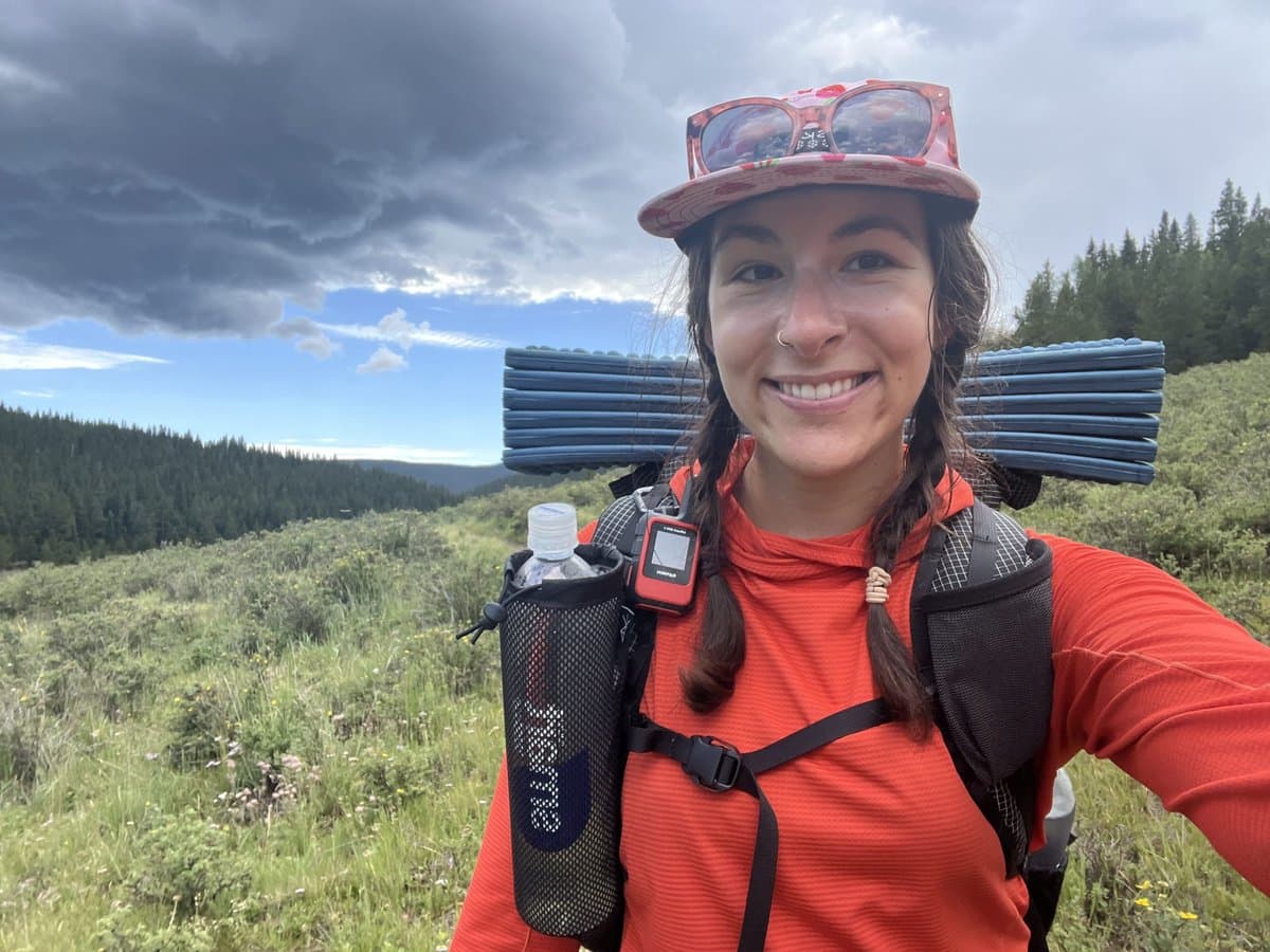 Garmin inReach Mini 3 Plus on hiking backpack with mountain trail background