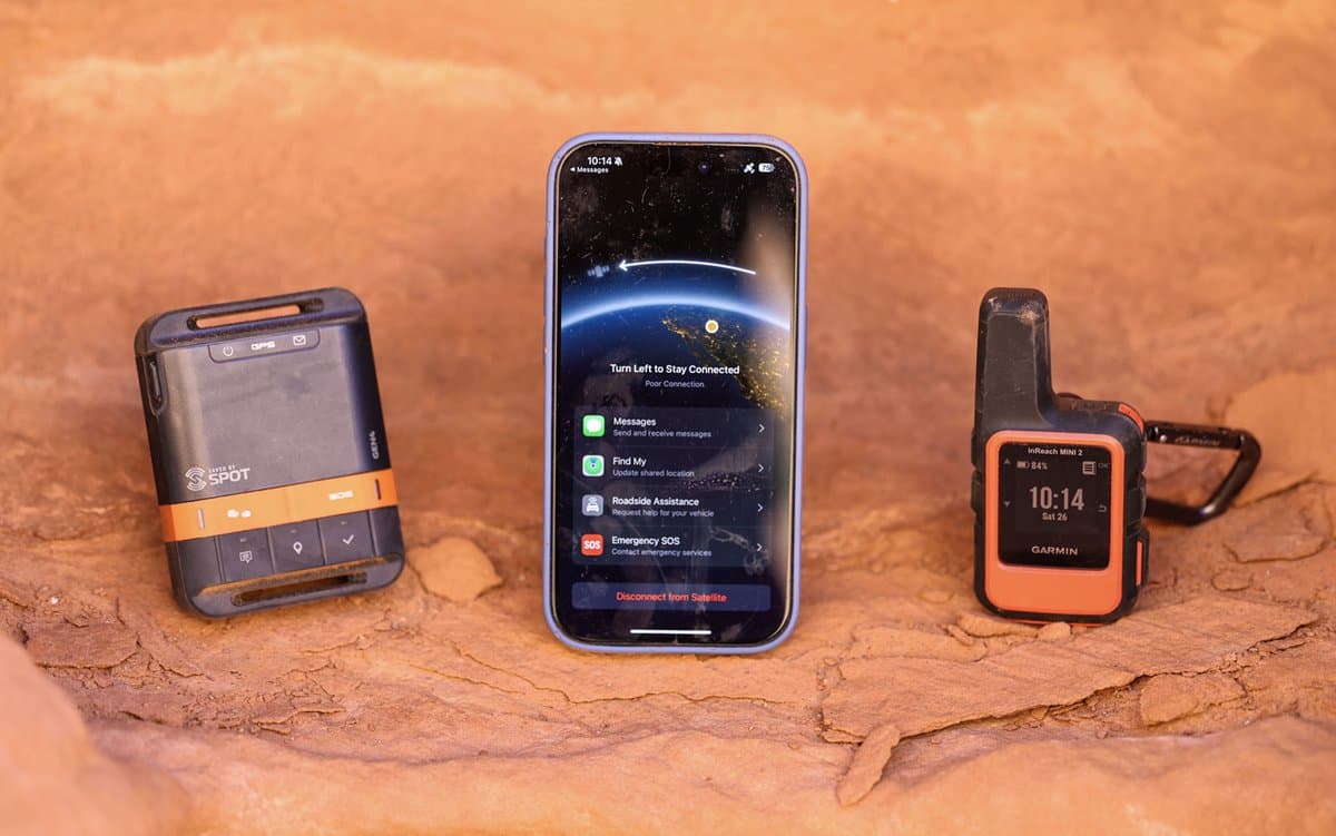 Satellite messenger devices laid out on rocky terrain with mountain backdrop